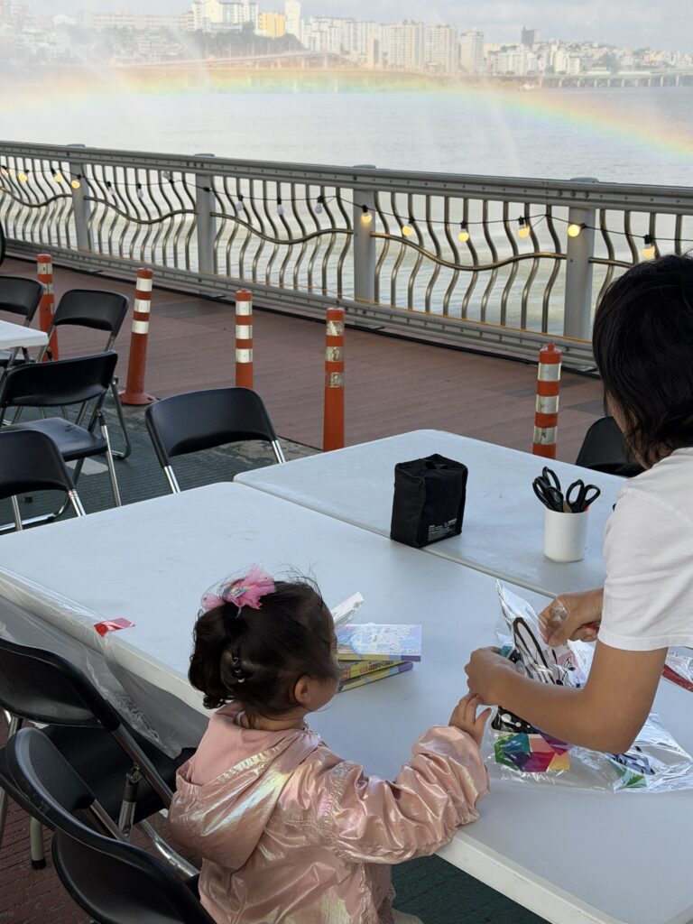 A child participating in an art activity with a rainbow visible over the water in the background.
