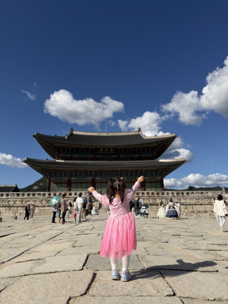 A child standing with arms raised in front of Geunjeongjeon throne hall at Gyeongbokgung Palace