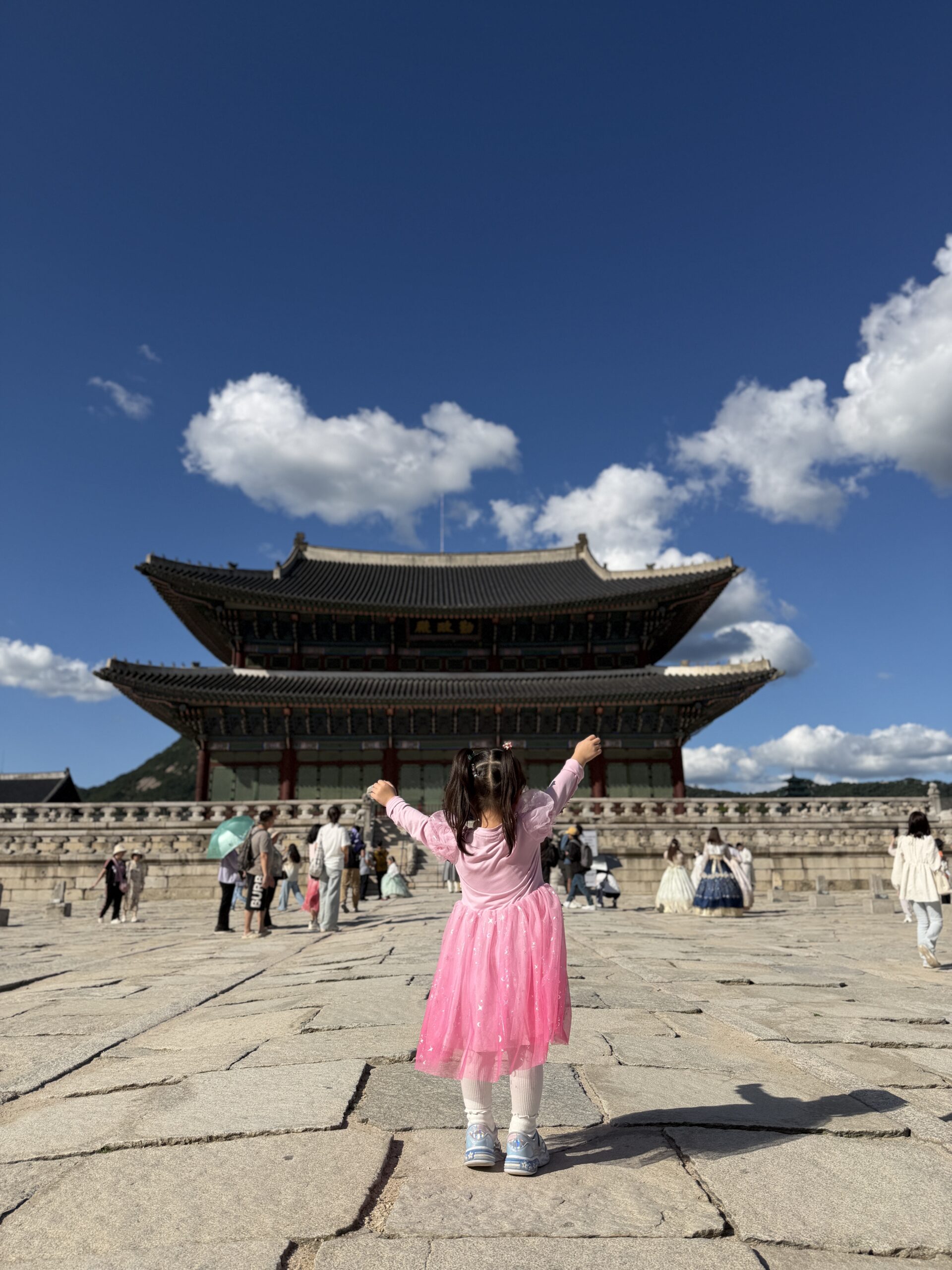 A child standing with arms raised in front of Geunjeongjeon throne hall at Gyeongbokgung Palace