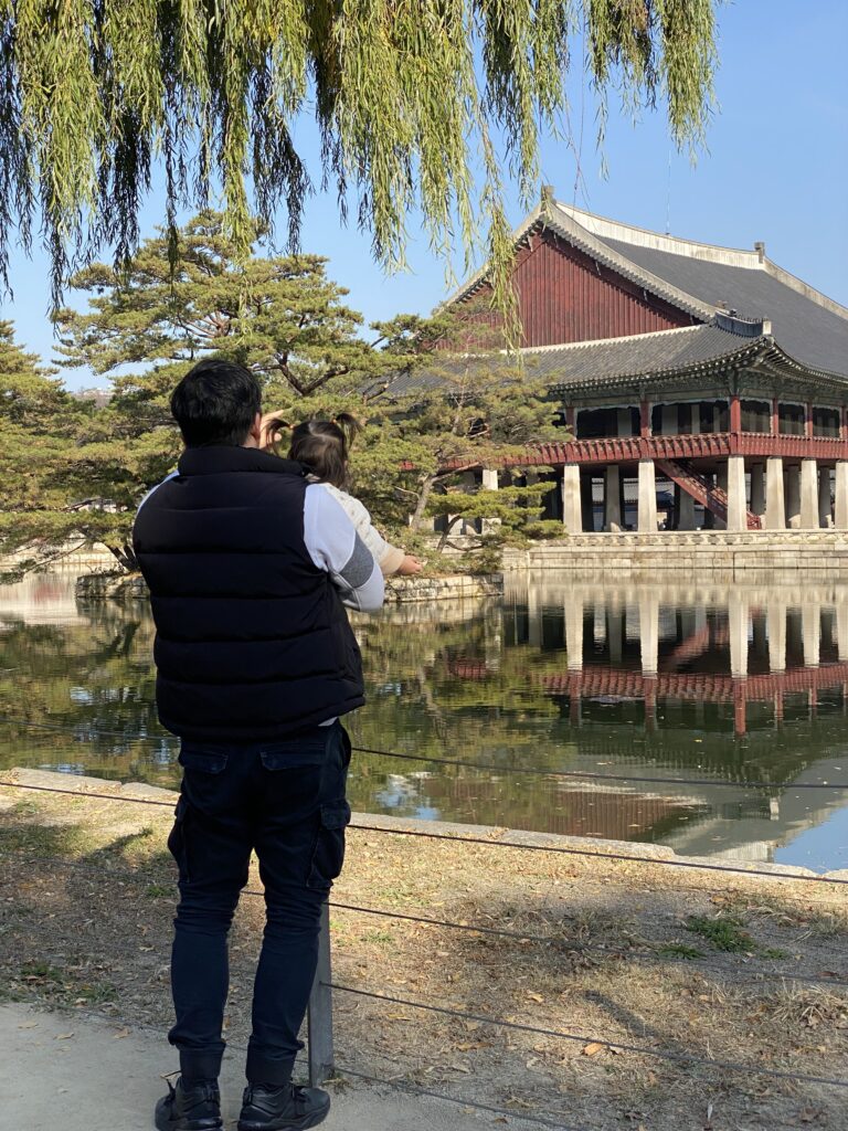 A father and child looking at Gyeonghoeru pavilion reflected on the pond at Gyeongbokgung Palace