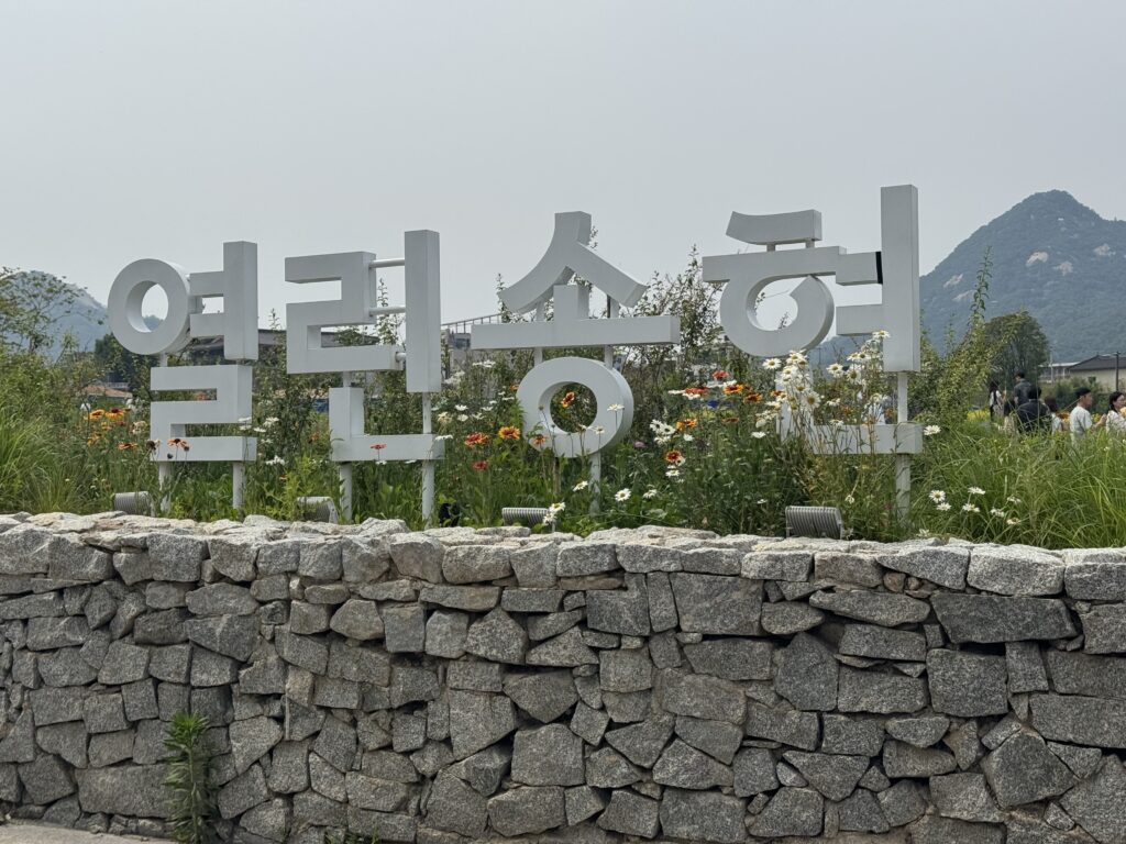 Songhyeon Green Plaza sign near Gyeongbokgung Palace with wildflowers and mountains