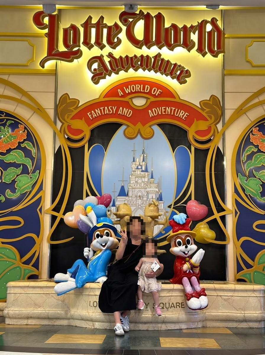 Family posing at the Lotte World Adventure entrance sign with Lotty and Lorry mascot characters in Seoul