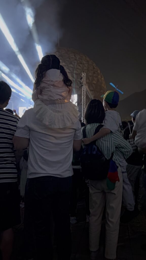 Family watching the evening fireworks and light show at Seoul Land, child on father's shoulders.