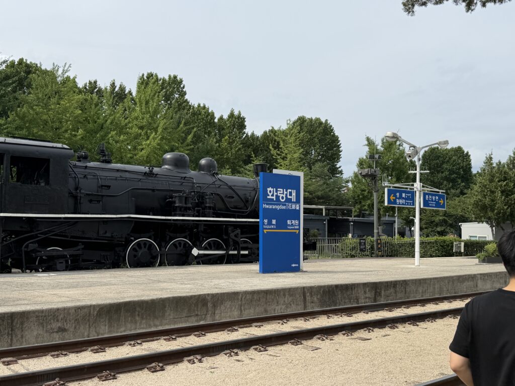 Old Hwarangdae Station name sign with a black steam locomotive on the tracks
