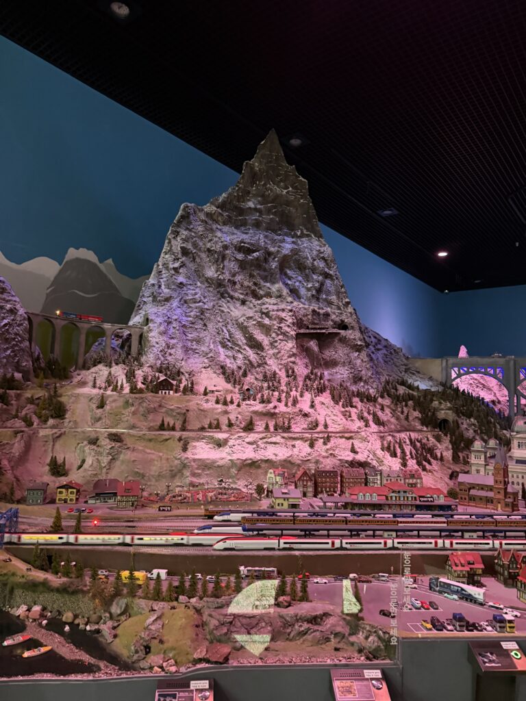 Large Matterhorn-style mountain miniature under pink lighting with multiple trains running below, Swiss Hall