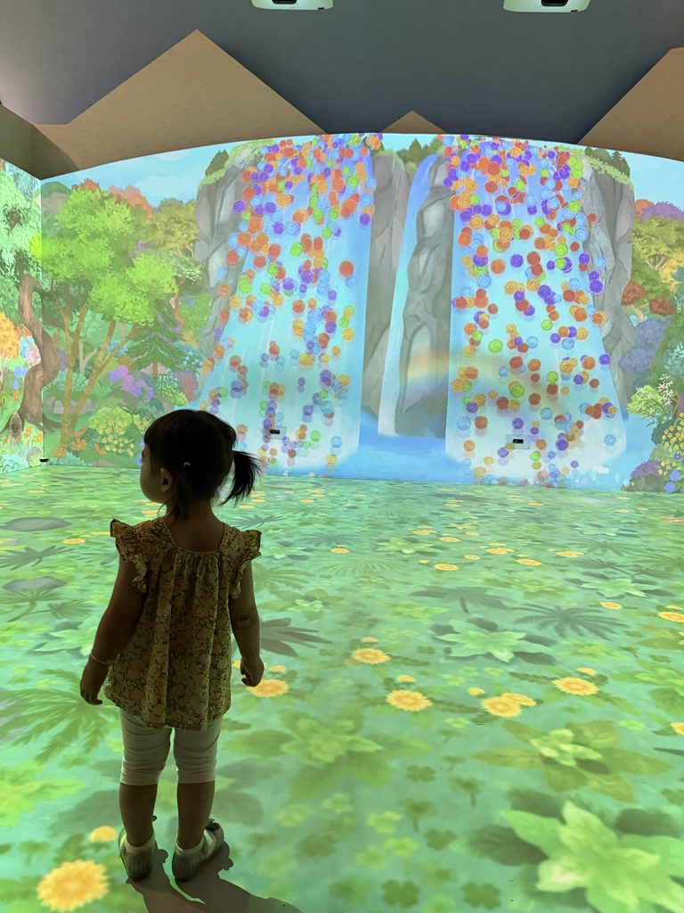 Child standing in a room-sized projection of a waterfall and flower meadow at the Children's Museum, Seoul