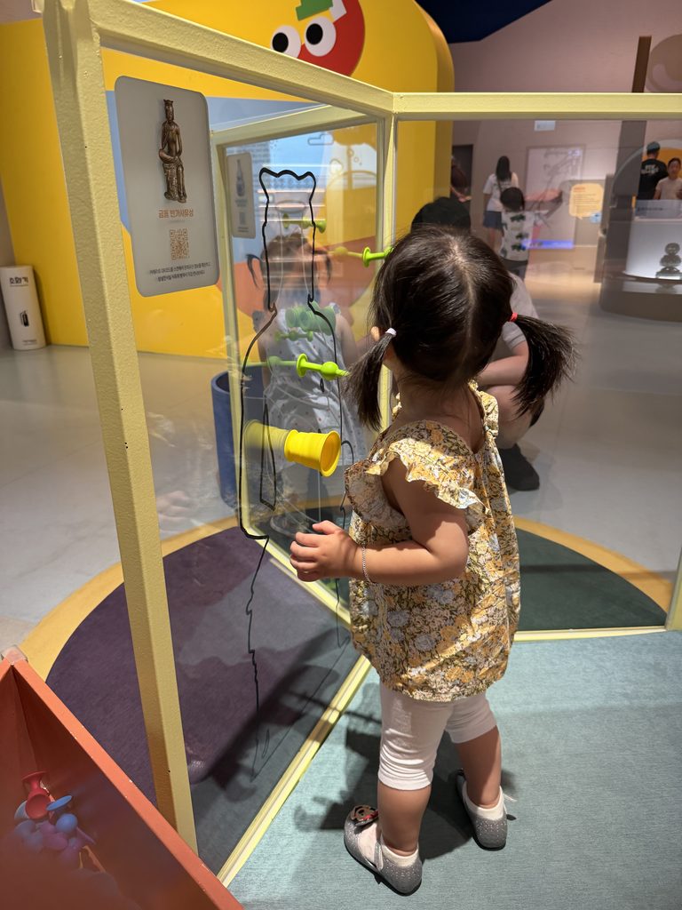 Toddler moving coloured suction pieces on a clear panel next to a museum artefact display, Children's Museum Seoul