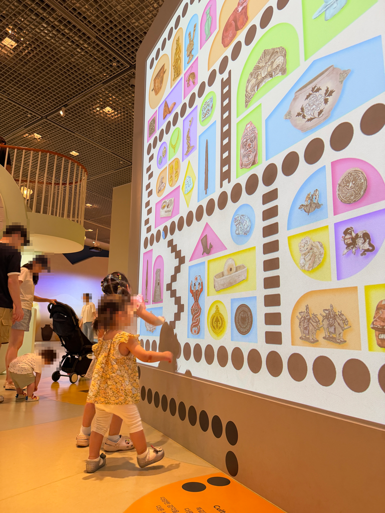 Toddler reaching toward a large projected media wall of illustrated Korean artefacts at the Children's Museum, Seoul