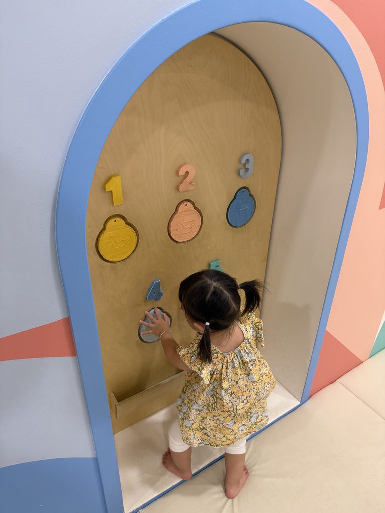 Toddler pressing raised numbers and animal tiles inside a padded arched alcove at the Children's Museum