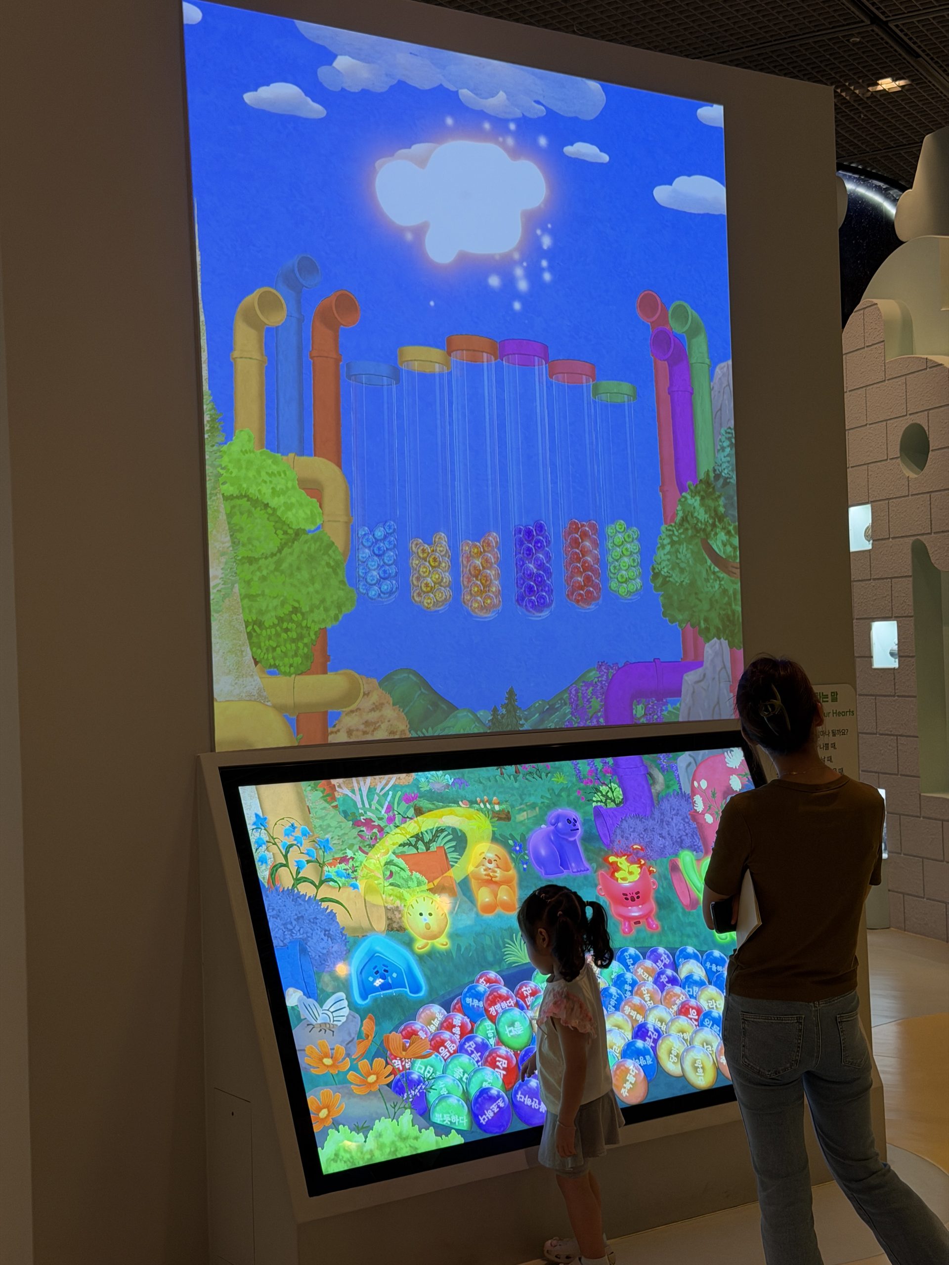 Young child and adult playing at a large interactive touchscreen with a rain and pipes animation, Children's Museum