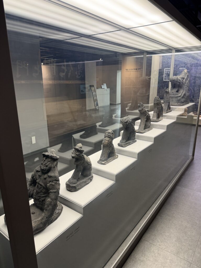A row of carved stone figures displayed on stepped plinths in a glass case at the Seoul City Wall Museum