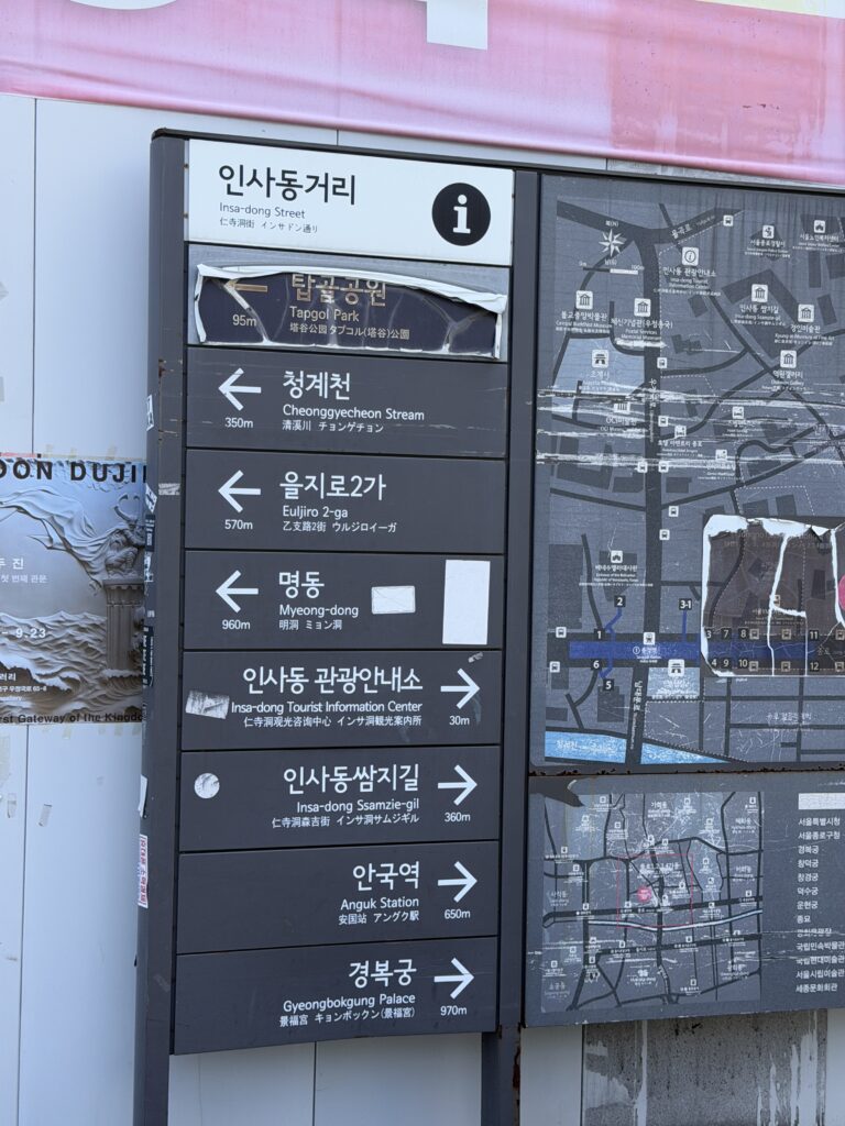 Multilingual direction sign on Insadong Street showing distances to Ssamzigil, Gyeongbokgung Palace, Tapgol Park and Anguk Station