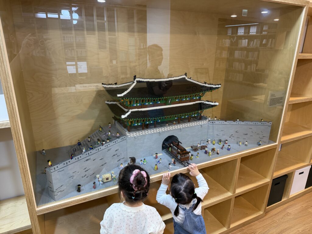 Two children looking at a Lego model of a Korean city gate and fortress wall in a display case at the Seoul City Wall Museum library