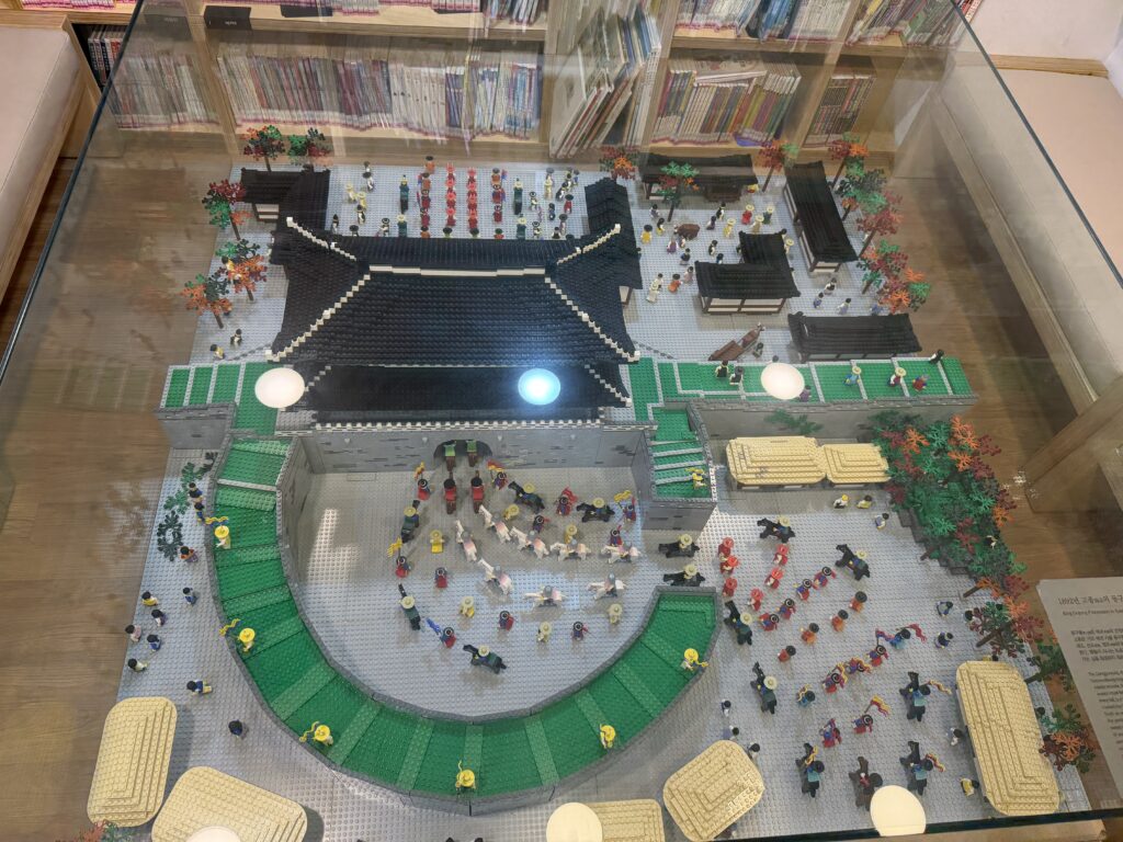 A detailed Lego model of a Korean palace courtyard filled with hundreds of minifigures, displayed at the Seoul City Wall Museum