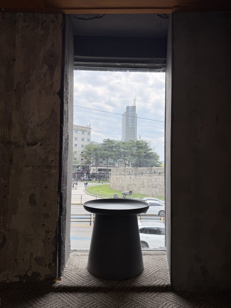 A low table in a floor-seating area of a Seoul cafe, framed by a concrete window opening looking out at the Seoul City Wall