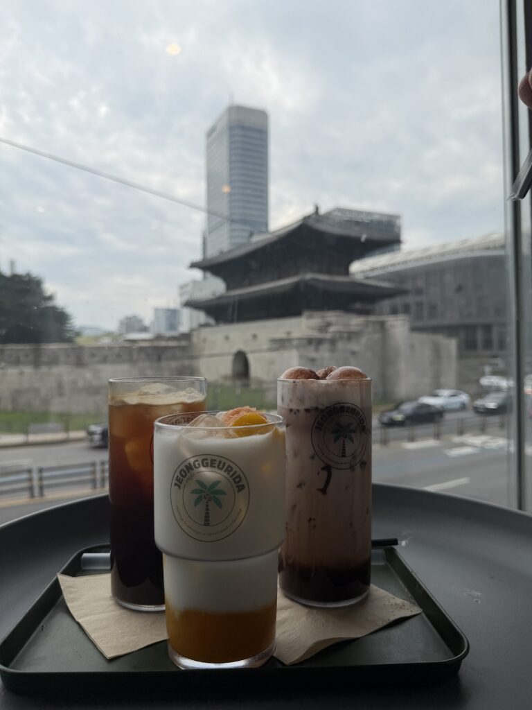 Three iced drinks on a tray beside a cafe window looking out at Heunginjimun Gate in Seoul