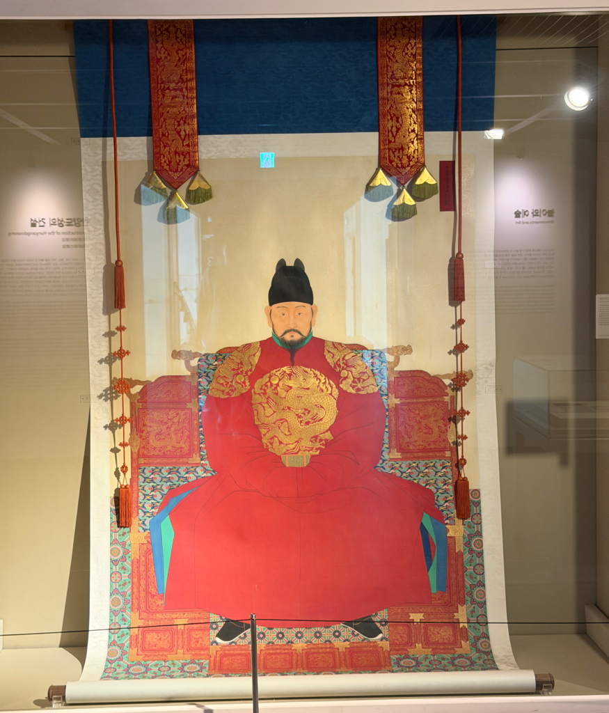 Portrait of King Taejo in red robes displayed in a glass case at the Seoul City Wall Museum