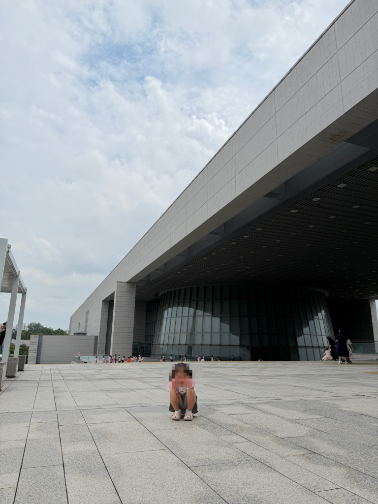 Child crouching on the wide plaza beneath the cantilevered main building of the National Museum of Korea, Seoul.