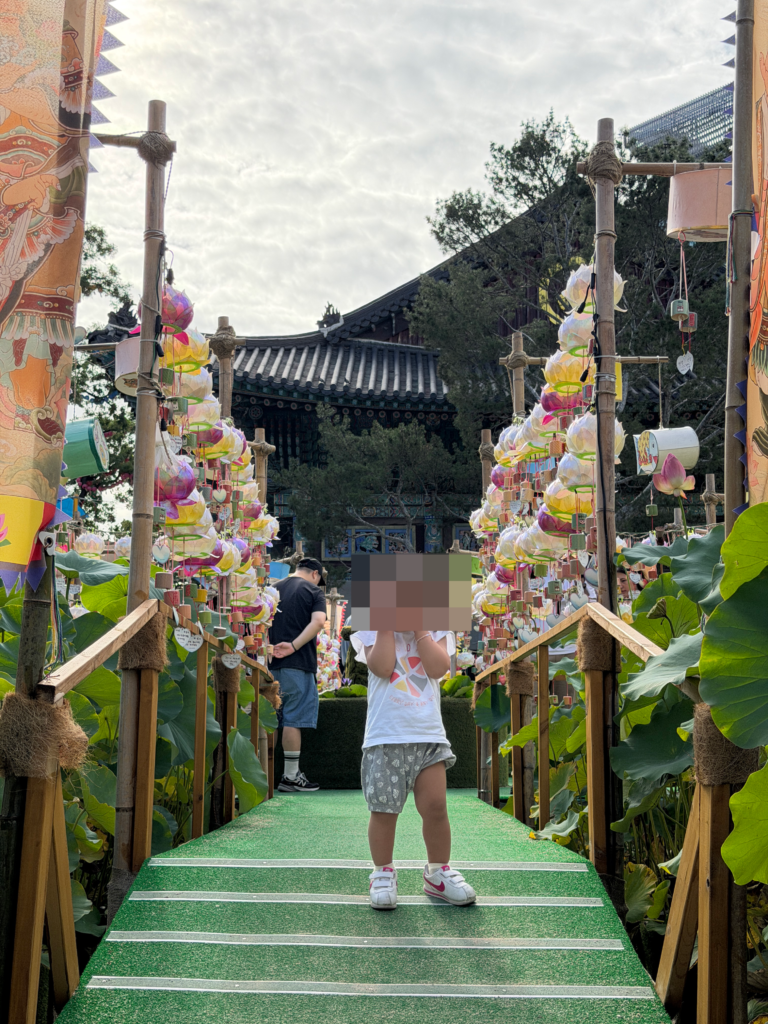 A young child walking through a tunnel of hanging red and orange paper lanterns at Jogyesa Temple in Seoul