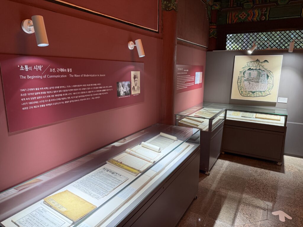  Bilingual exhibition panel titled "The Beginning of Communication" with glass cases of historic documents at the Korea Postal Museum