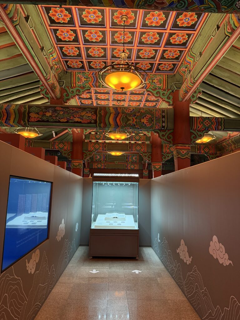 Interior of the Korea Postal Museum showing modern display cases beneath the original painted wooden ceiling of the historic post office building