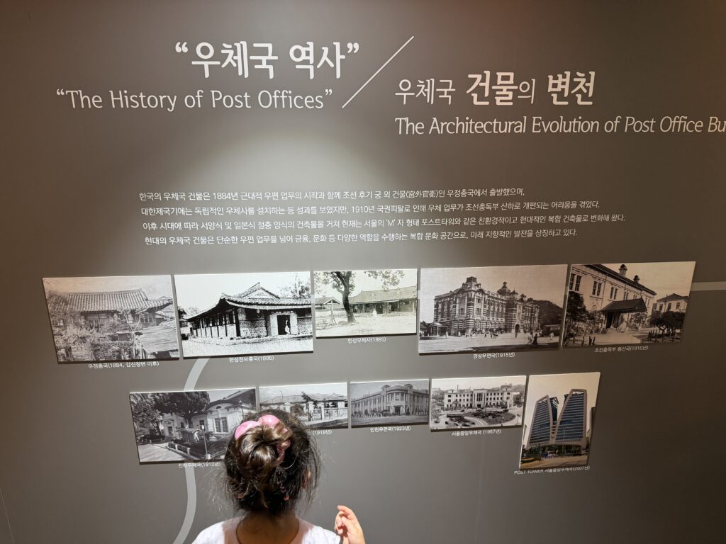 A young child pointing at a wall display showing the architectural changes to Korea's first post office building