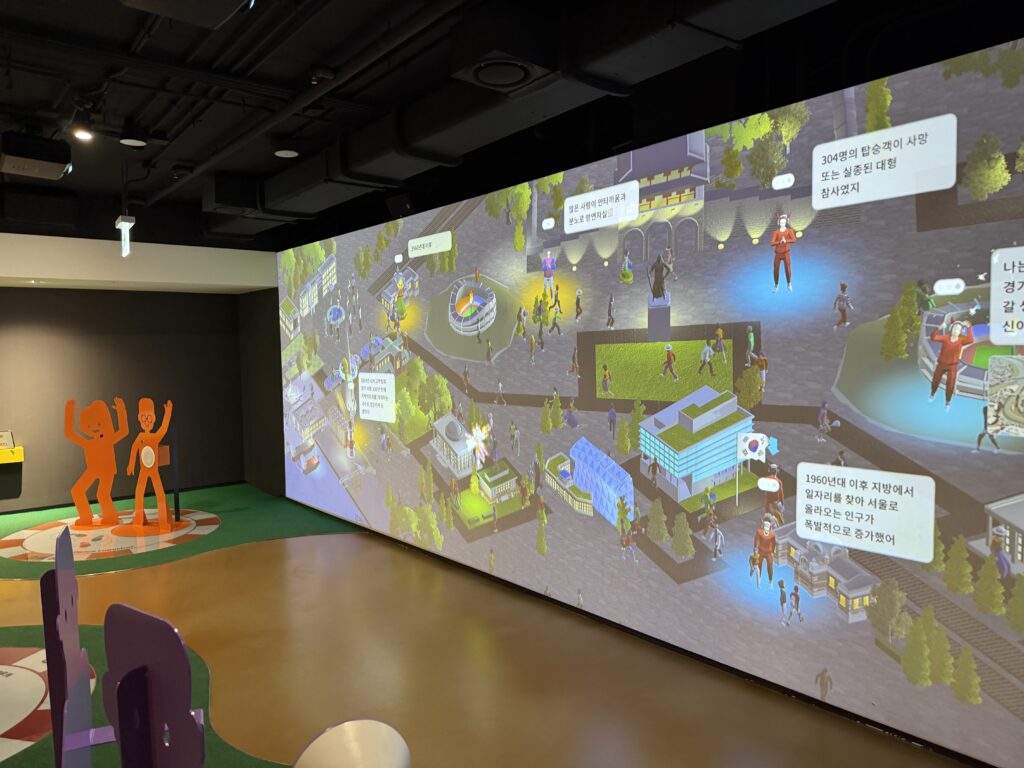 Large projection wall showing an animated Korean city square filled with characters created by visiting children