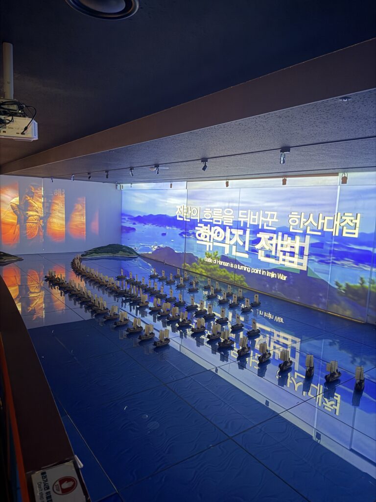 Floor model of the Battle of Hansan showing miniature ships in crane-wing formation under a projected sea at The Story of Admiral Yi Sunshin