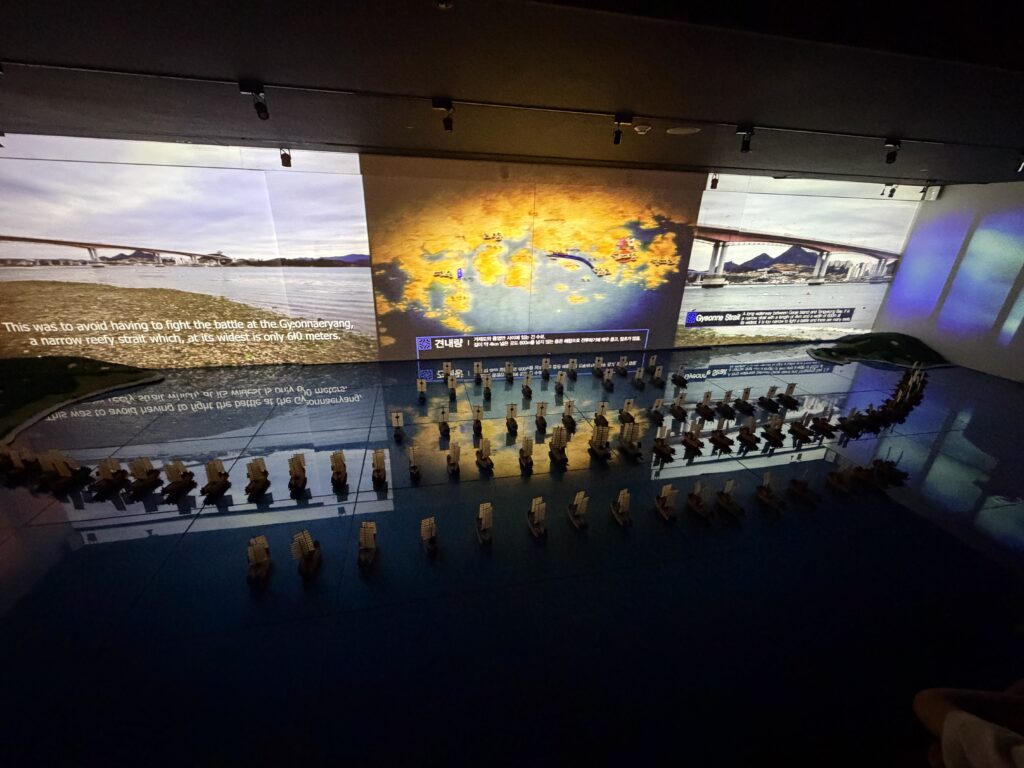 English narration subtitle projected above the Battle of Hansan model explaining the Gyeonnaeryang strait tactics