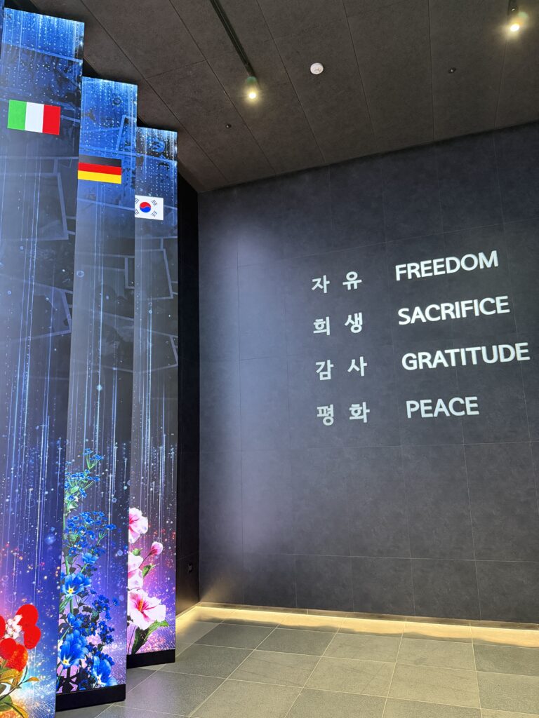 Wall reading Freedom, Sacrifice, Gratitude and Peace in Korean and English beside illuminated LED national pillars in Freedom Hall